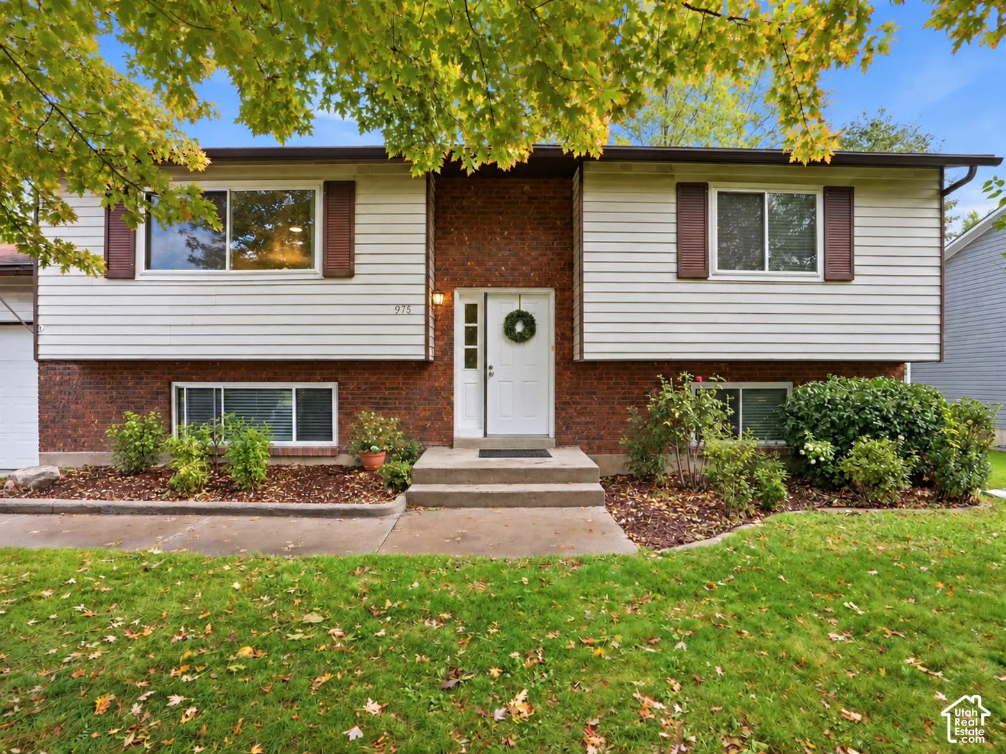 Split-level exterior featuring a brick and horizontal siding facade, shuttered windows, concrete entryway, and manicured landscaping
