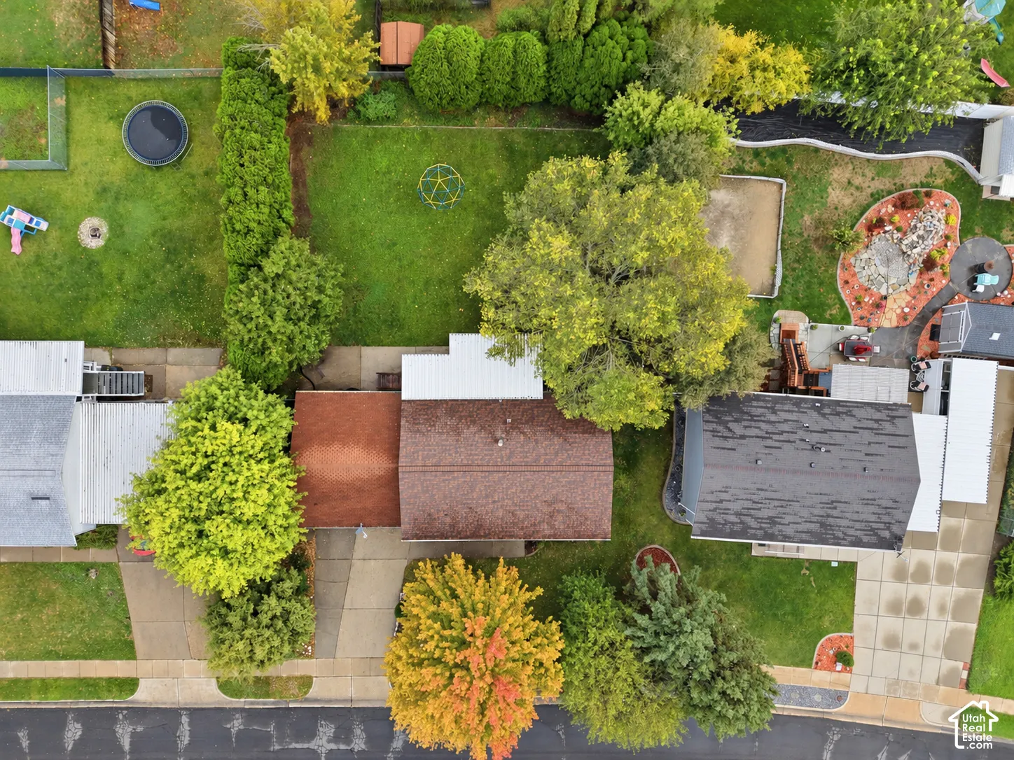 Aerial perspective featuring a spacious backyard, mature landscaping, concrete driveway, and established tree canopy