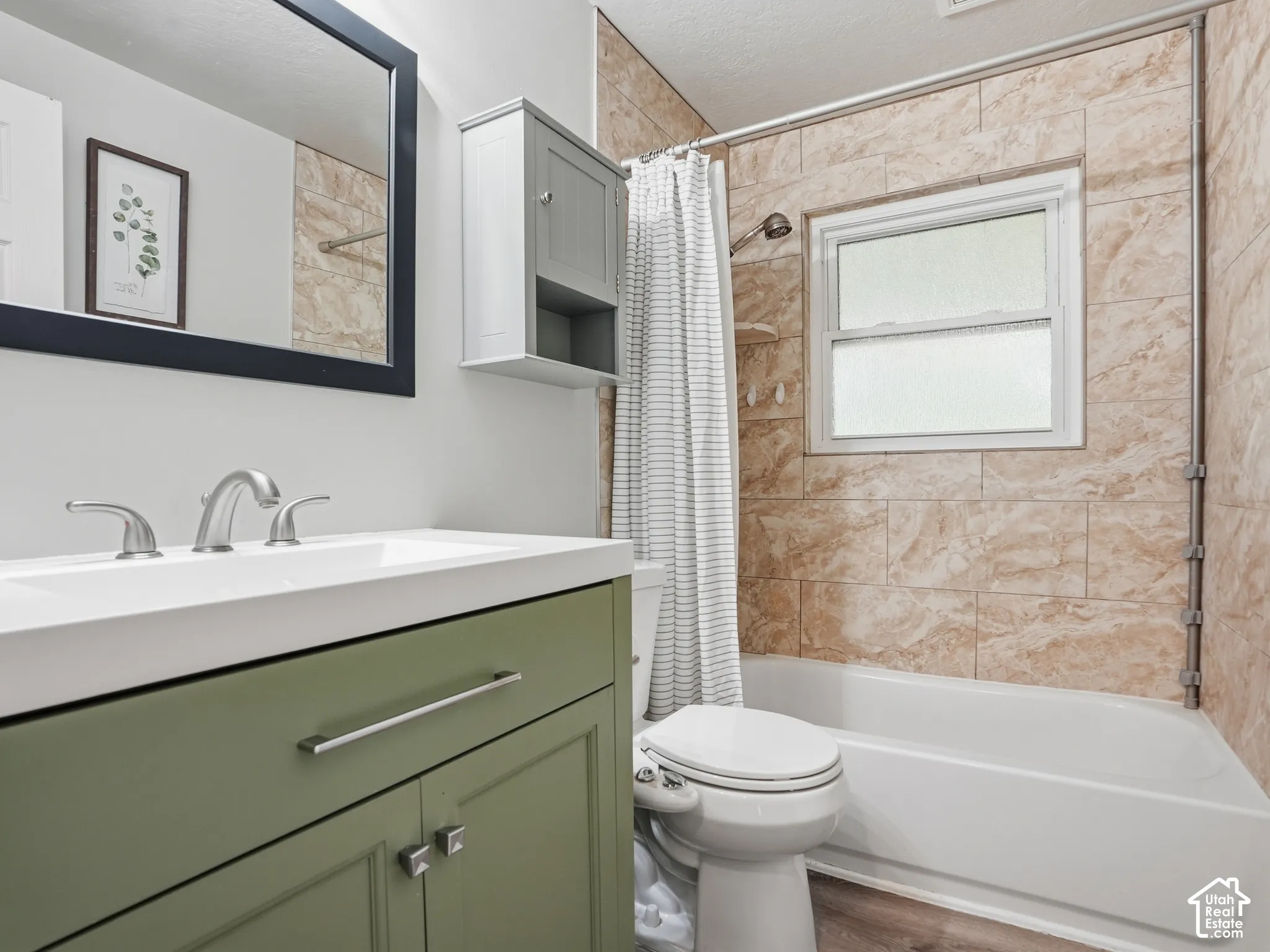 Bathroom featuring a sage green vanity with a rectangular sink, wall-mounted medicine cabinet, framed mirror, and tub-shower combination with floor-to-ceiling stone-patterned tile