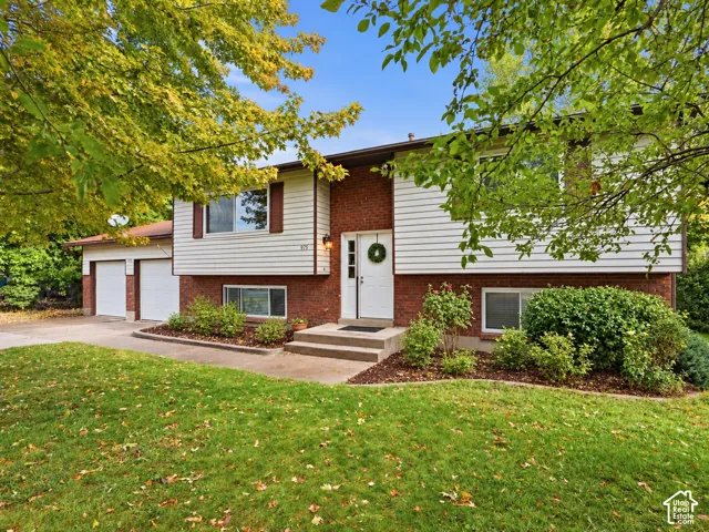 Split-level exterior featuring a brick and horizontal siding facade, two-car garage, manicured landscaping, and concrete walkway
