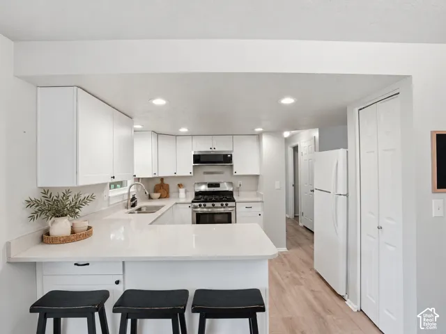 Kitchen featuring white shaker-style cabinetry, solid-surface countertops, a stainless steel gas range with overhead microwave, and wood-finish flooring