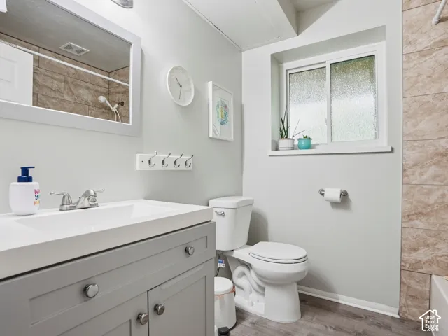 Bathroom featuring a gray vanity with an integrated sink, polished chrome faucet, wood-finish flooring, and tile-surround shower area
