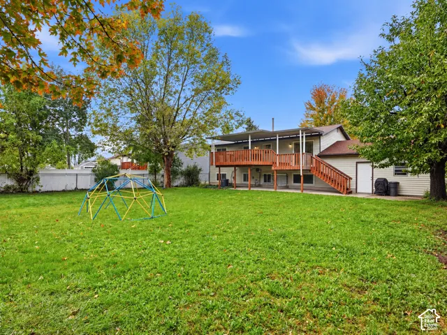Backyard featuring a grass lawn, mature trees, wood deck with stairs, and white privacy fencing