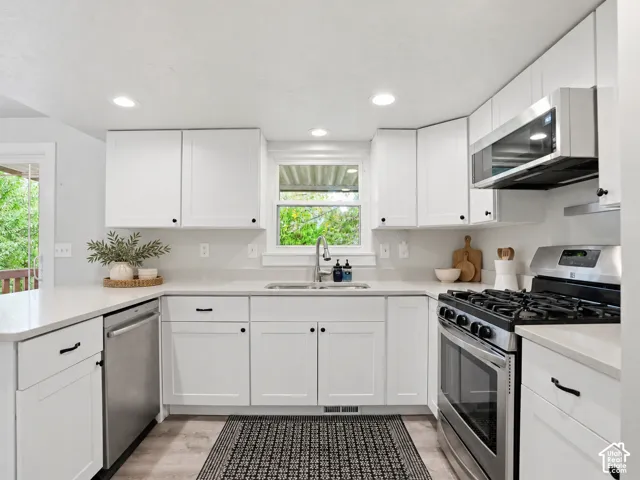 Kitchen featuring white shaker-style cabinetry, solid-surface countertops, recessed lighting, and stainless steel appliances