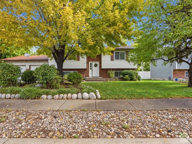 Split-level exterior featuring brick and horizontal siding, an attached two-car garage, and a landscaped front yard with stone border edging