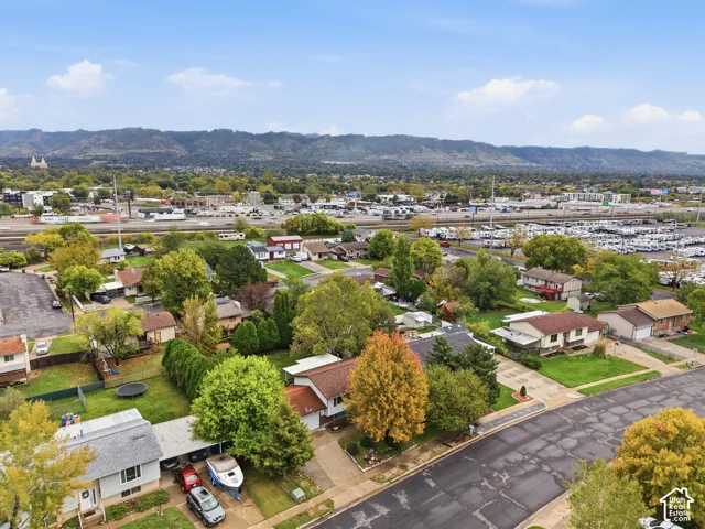 Aerial perspective of a suburban neighborhood featuring mature trees, landscaped lawns, asphalt streets, and a mountainous backdrop