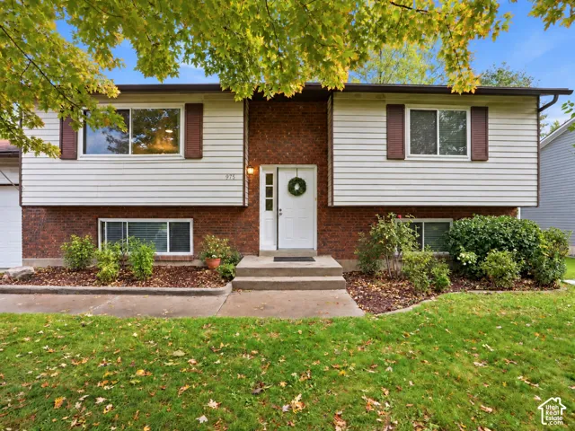 Split-level exterior featuring a brick and horizontal siding facade, shuttered windows, concrete entryway, and manicured landscaping