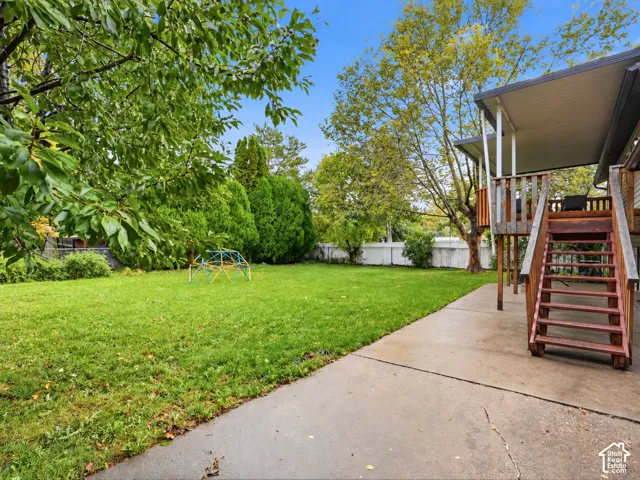 Backyard featuring a manicured lawn, concrete patio, elevated wooden deck with stairs, and perimeter fencing