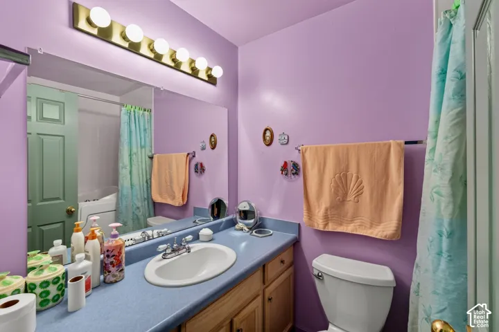 Bathroom featuring a wood-finish vanity cabinet, solid-surface countertop with an integrated oval sink, full-width wall mirror, and five-bulb brass-finish vanity light