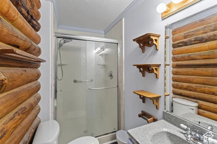 Bathroom featuring log-style wall cladding, a glass-enclosed shower, stone-finish vanity countertop with an integrated sink, and tiered wall-mounted shelving