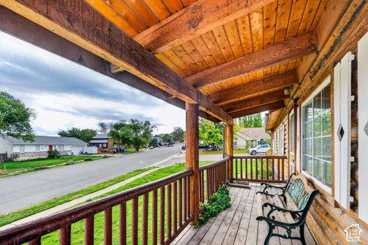 Covered front porch featuring exposed timber beam ceiling, log-style railing, and plank flooring