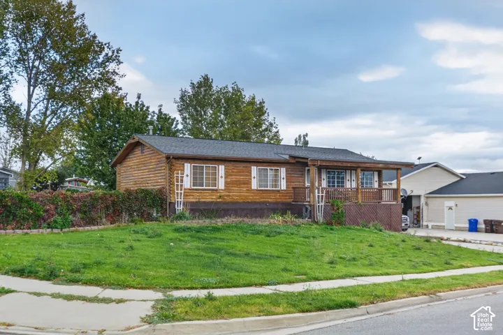 Log cabin exterior featuring wood siding, a covered front porch, asphalt shingle roofing, and white shutters