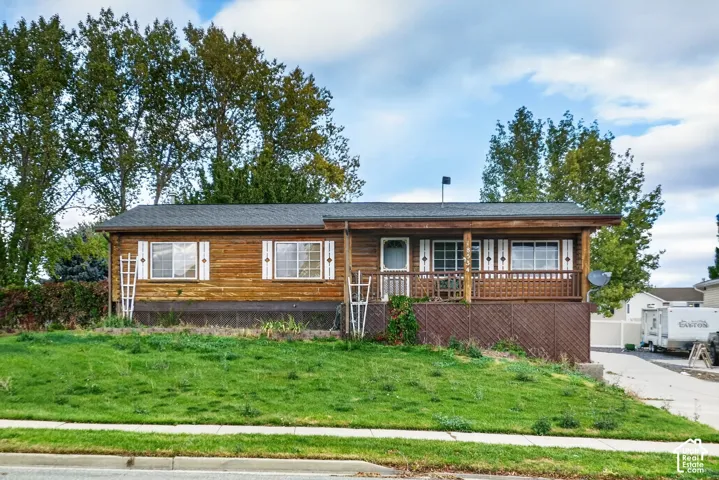 Single-story exterior featuring log-style siding, a covered front porch with wooden railing, lattice skirting, and white window shutters
