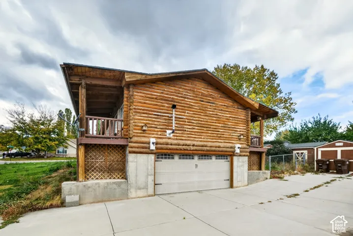 Log cabin exterior featuring horizontal log siding, a concrete foundation, a multi-car garage with overhead doors, a covered balcony, and lattice privacy screening