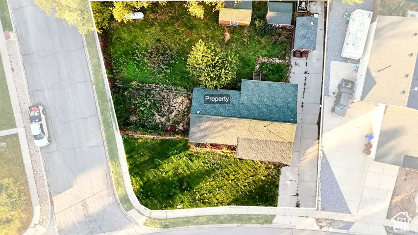 Aerial perspective of a property featuring an expansive lawn, concrete driveway, and established trees