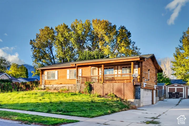 Log-style exterior featuring a covered front porch, lattice skirting, attached garage, and concrete driveway