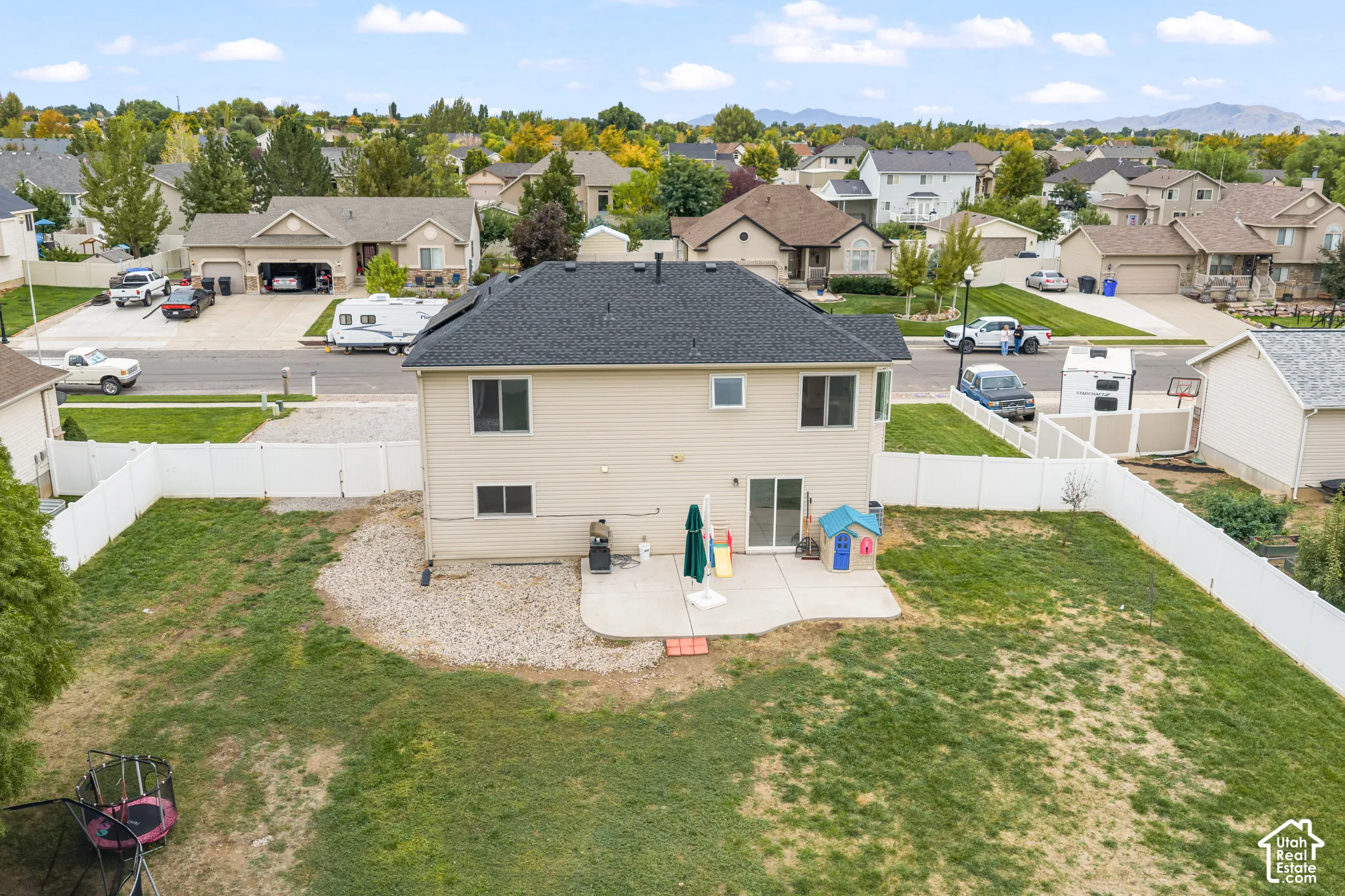 Two-story residence featuring light-toned horizontal siding, a dark-shingled roof, a concrete patio, and a fully enclosed vinyl fence