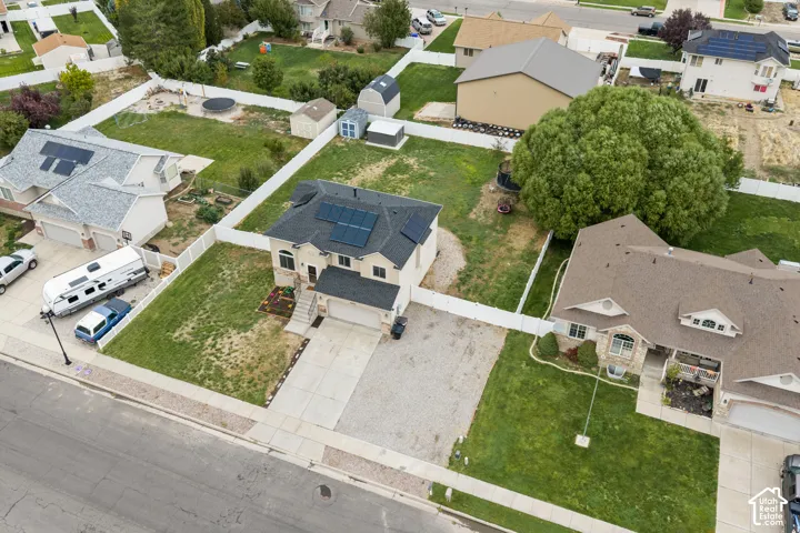 Two-story residence featuring a shingled roof with integrated solar panels, a concrete driveway, a gravel parking area, and a fenced yard