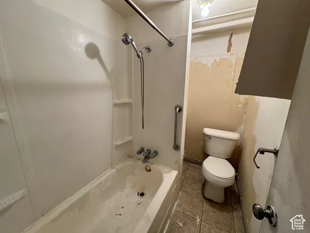Bathroom featuring a composite tub surround with integrated shelving, chrome shower hardware, metal safety grab bar, two-piece toilet, and tile flooring