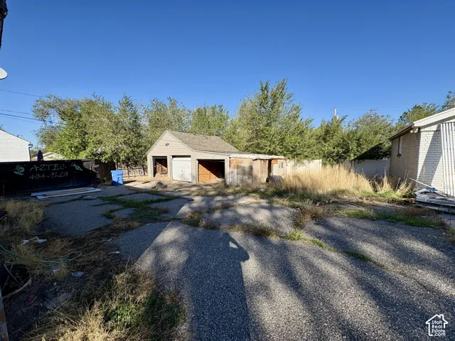 Detached garage building with a shingled roof, concrete driveway, and mature perimeter trees