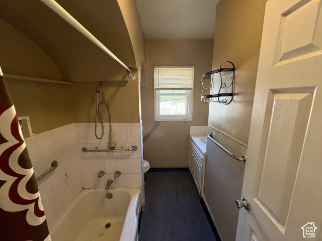 Bathroom featuring a recessed bathtub with white tile surround, handheld shower fixture, built-in vanity cabinet, and wall-mounted metal grab bars