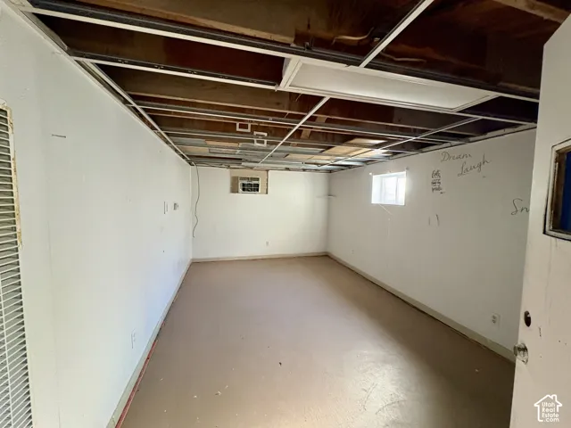 Unfinished interior space featuring exposed ceiling joists, white-painted walls, solid flooring, and inset windows