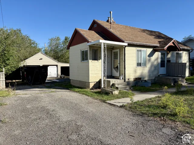 Single-story residence featuring light-colored siding, a pitched roof, gravel driveway, and a detached garage