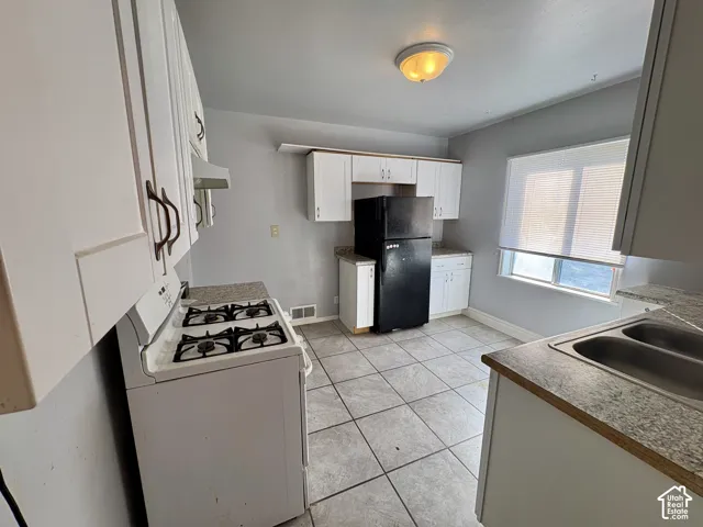 Kitchen featuring white cabinetry, stone-finish countertops, tiled flooring, a gas range, and a dual-basin sink