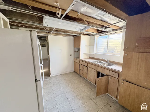 Kitchen featuring wood-finish cabinetry, stainless steel dual-basin sink, tiled flooring, and a single-hung window