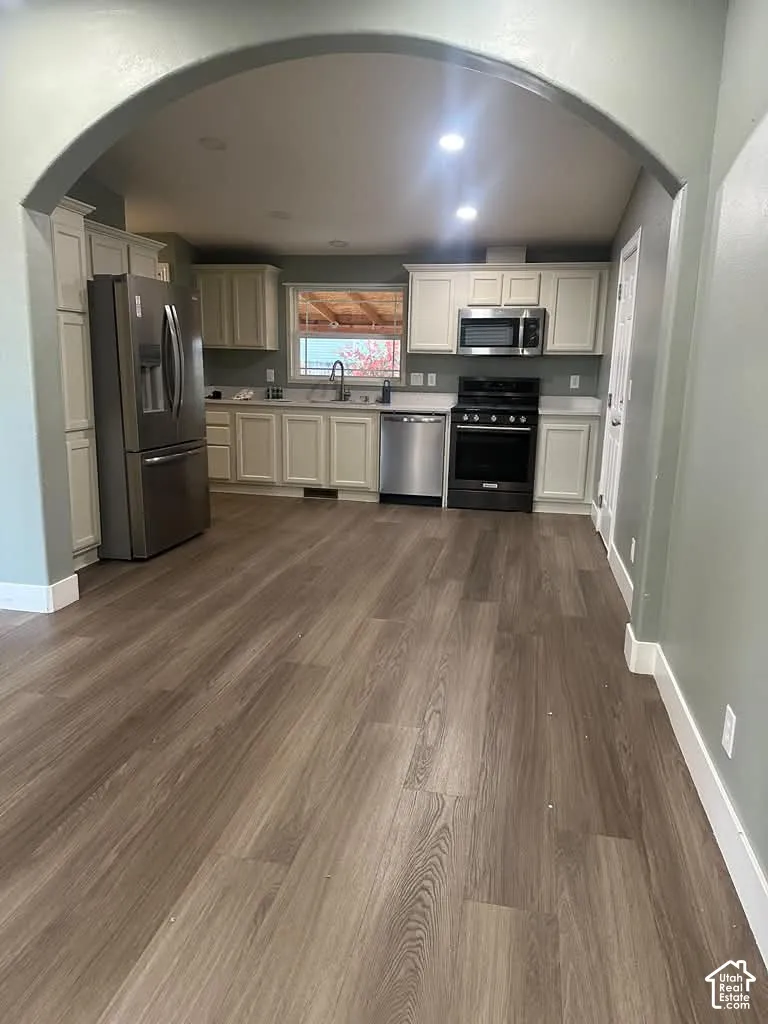 Kitchen featuring an arched entryway, wood-finish flooring, white cabinetry, stainless steel appliances, and recessed lighting