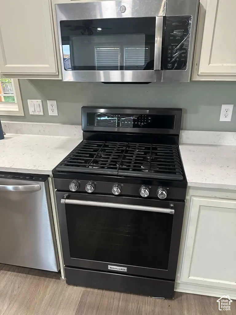 Kitchen featuring light-toned cabinetry, solid-surface countertops, black gas range, stainless steel over-the-range microwave, and wood-finish flooring