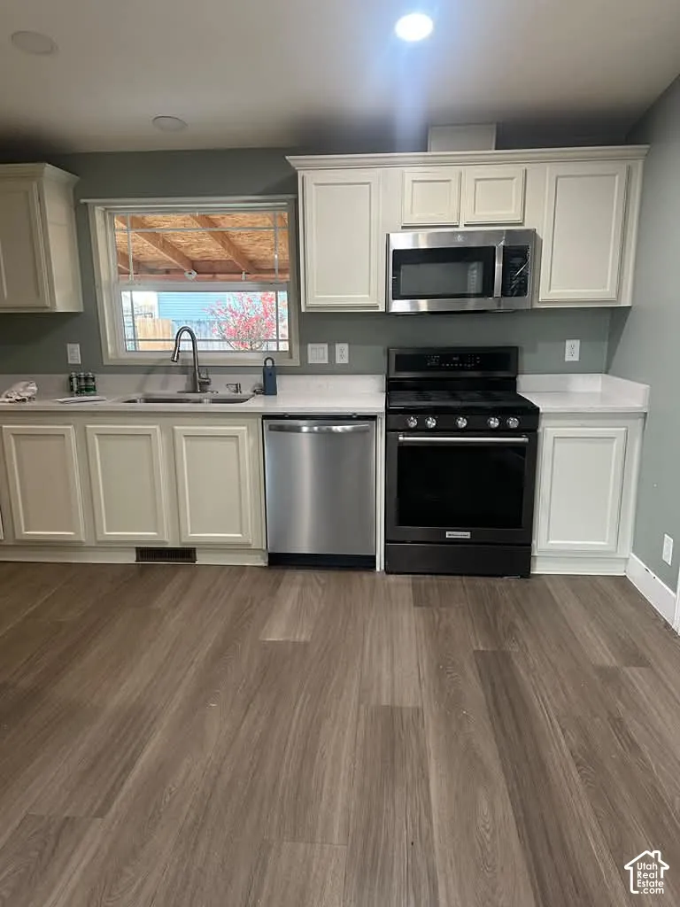 Kitchen featuring off-white cabinetry, solid surface countertops, stainless steel appliances, and wood-finish flooring