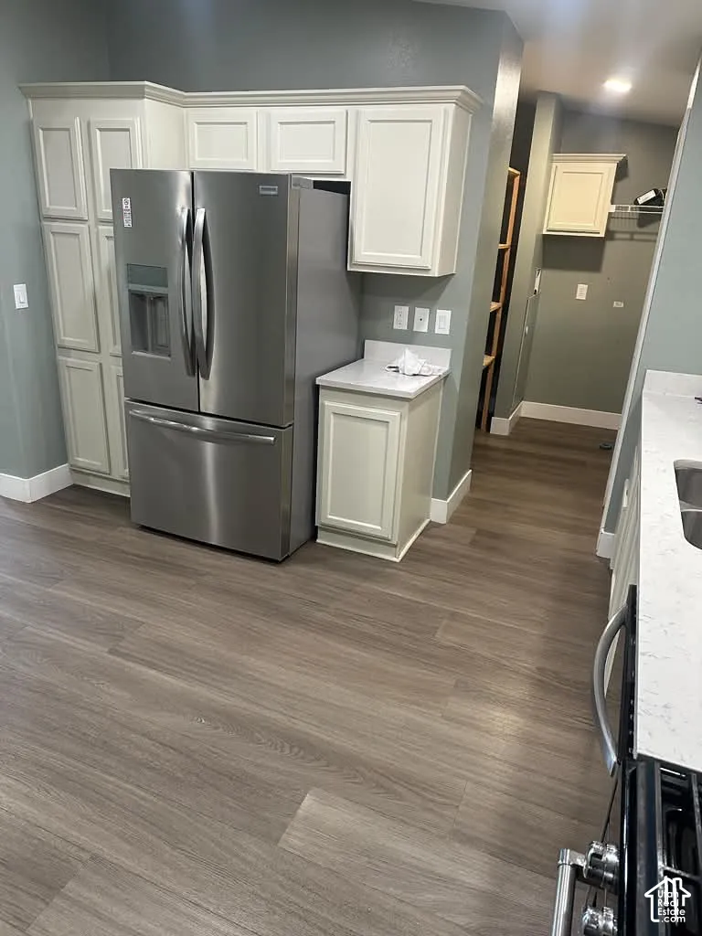 Kitchen featuring custom shaker-style cabinetry, wood-finish flooring, stone-surface countertops, and stainless steel refrigerator