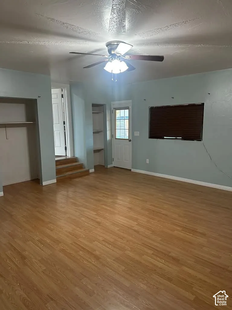 Interior space featuring wood-finish flooring, recessed wall shelving, a glass-panel exterior door, and a multi-blade ceiling fan with integrated lighting
