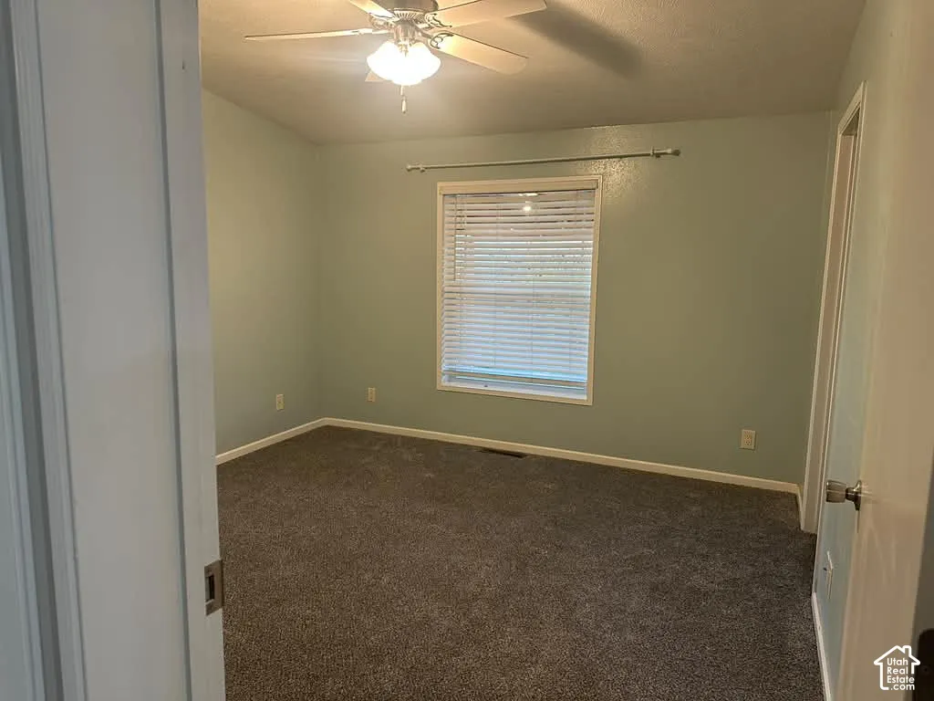 Interior space featuring neutral-toned carpeting, a ceiling fan with integrated light fixture, and a window with horizontal blinds