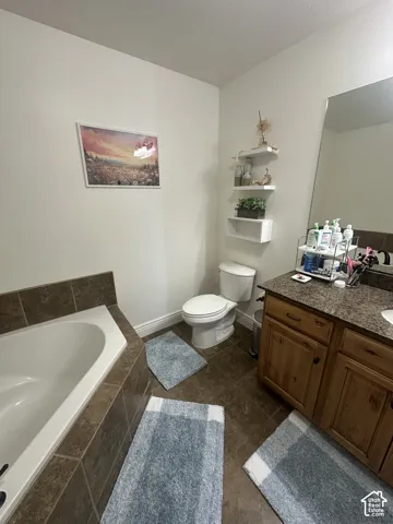 Soaking tub featuring tile surround, vanity with stone-composite countertop, and built-in wall shelving