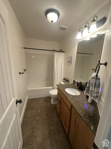 Bathroom featuring a vanity with stone-finish countertop, undermount oval sink, wooden cabinetry, large wall-mounted mirror, and tile flooring