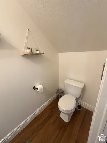 Restroom featuring wood-finish flooring, a two-piece white toilet, and a matte black toilet paper holder