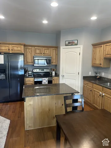 Kitchen featuring custom wood cabinetry, a central island with a stone-surface countertop, recessed ceiling lighting, and wood-finish flooring