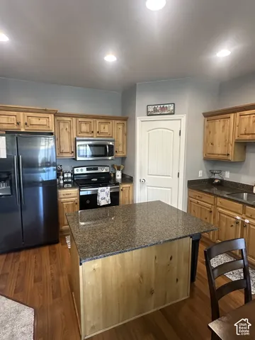 Kitchen featuring custom wood cabinetry, a central island with stone-surface countertop, wood-finish flooring, and integrated stainless steel appliances