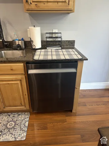 Kitchen featuring stone-finish countertops, stainless steel dishwasher, wood cabinetry, and wood-finish flooring