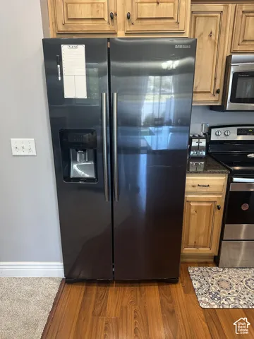 Black stainless steel side-by-side refrigerator featuring an integrated water and ice dispenser, dark-toned cabinetry with natural wood finish, and wood-finish flooring