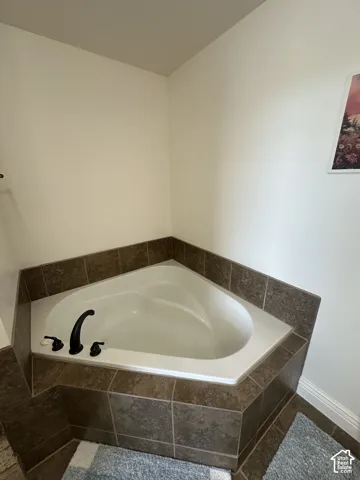 Corner soaking tub featuring a white acrylic basin and dark brown tile surround with integrated black hardware