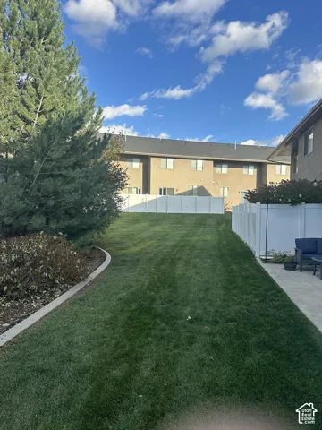 Backyard featuring a grass lawn, mature pine tree, concrete paver patio, and white vinyl privacy fencing