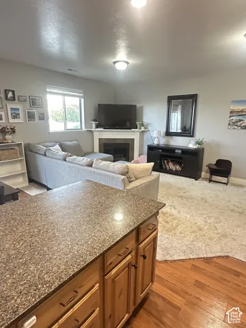 Kitchen featuring a speckled stone-finish countertop and wood cabinetry, paired with a living area including a fireplace with a white mantel and a window