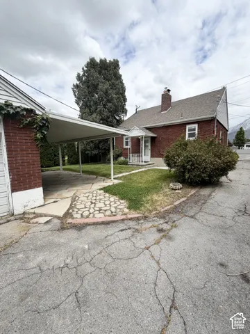 Brick exterior residence featuring a covered carport, stone-laid walkway, and chimney