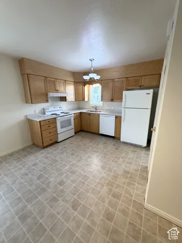 Kitchen featuring wood cabinetry, white appliances, integrated light valance, and neutral tile flooring