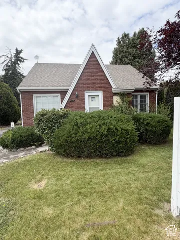 Brick exterior featuring a steeply pitched A-frame gable, shingle roof, multi-pane windows, and a paved walkway