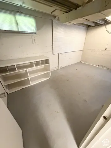 Lower-level utility area featuring painted concrete walls, a horizontal sliding window, and integrated pegboard wall panels