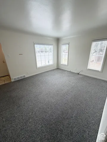 Neutral-toned interior space featuring wall-to-wall carpeting, three multi-pane windows with horizontal blinds, and smooth-finish walls